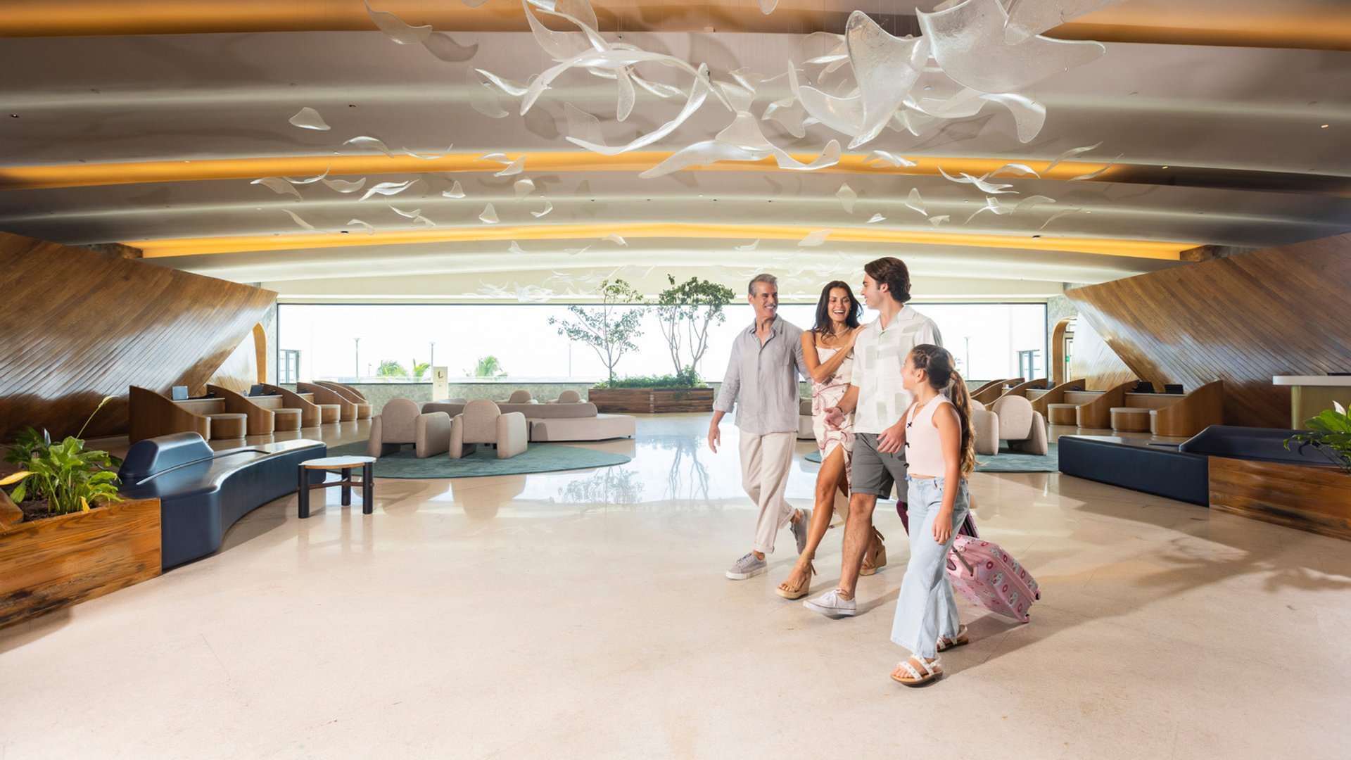 Family walks through a modern, spacious hotel lobby with seating areas and art installations overhead.