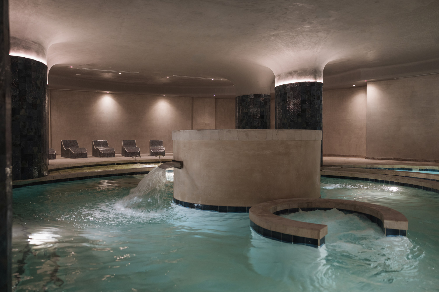 a pool with a fountain and chairs in the background